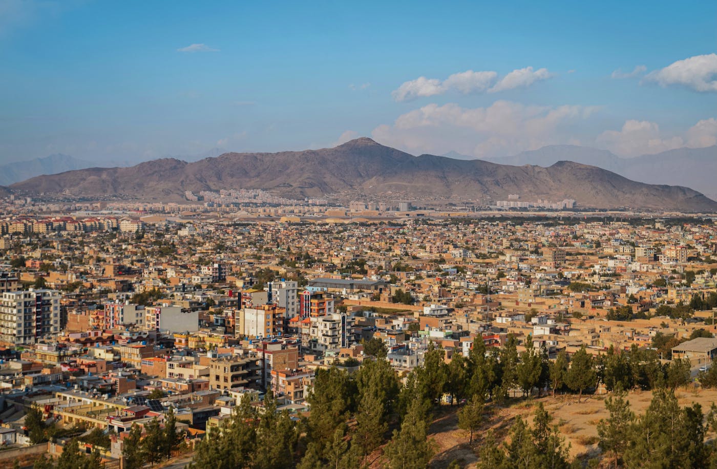 Wide cityscape of Kabul in a mountain valley under a clear sky — urban environment, air, and landscape.