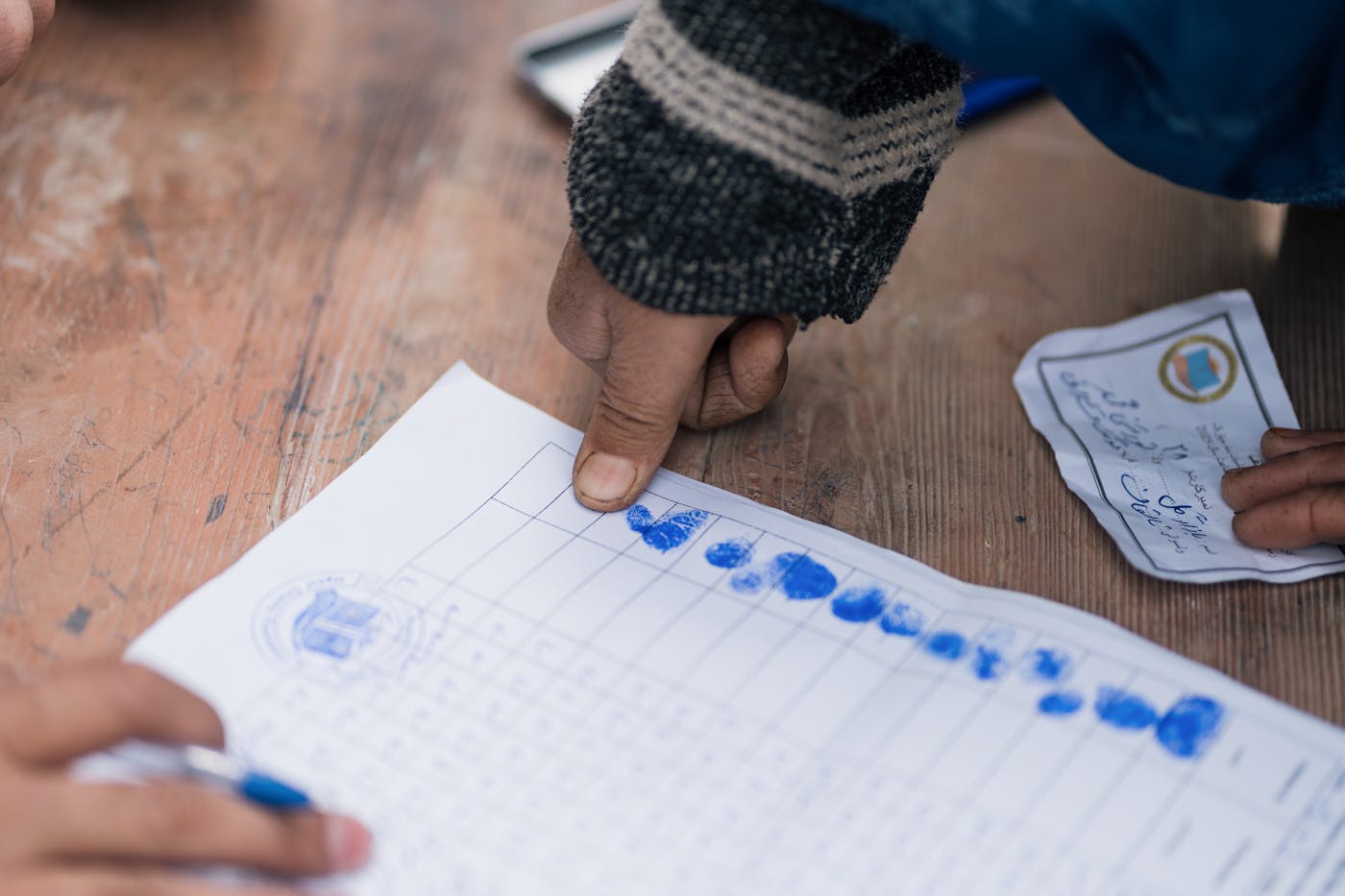 Close-up of a thumb pressing blue ink onto an official registration grid — participation and verification.
